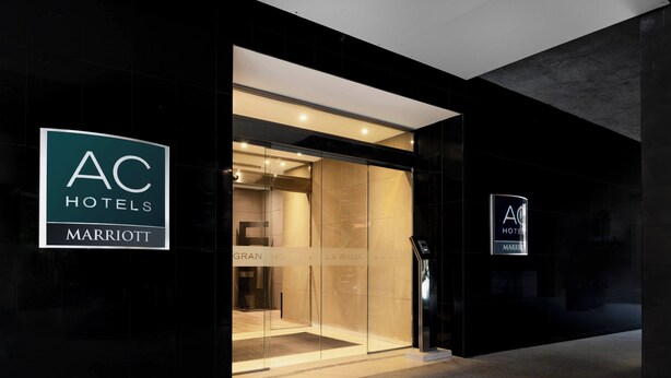 L’entrée d’un hôtel, avec une porte en verre, une enseigne indiquant « AC Hotels Marriott » et un écran numérique.