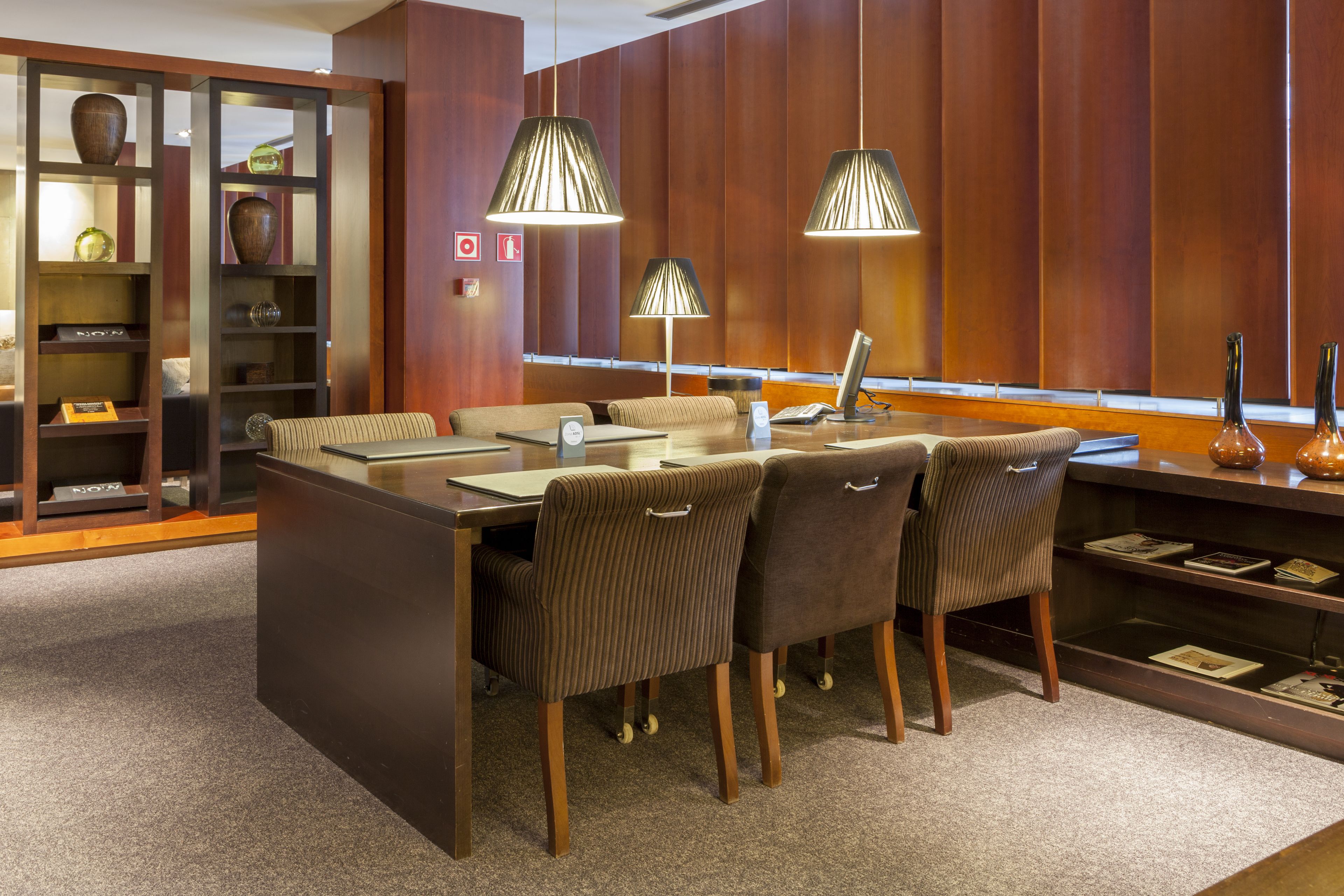 A modern dining area with a central island, cushioned chairs, pendant lighting, and a wooden panel wall.