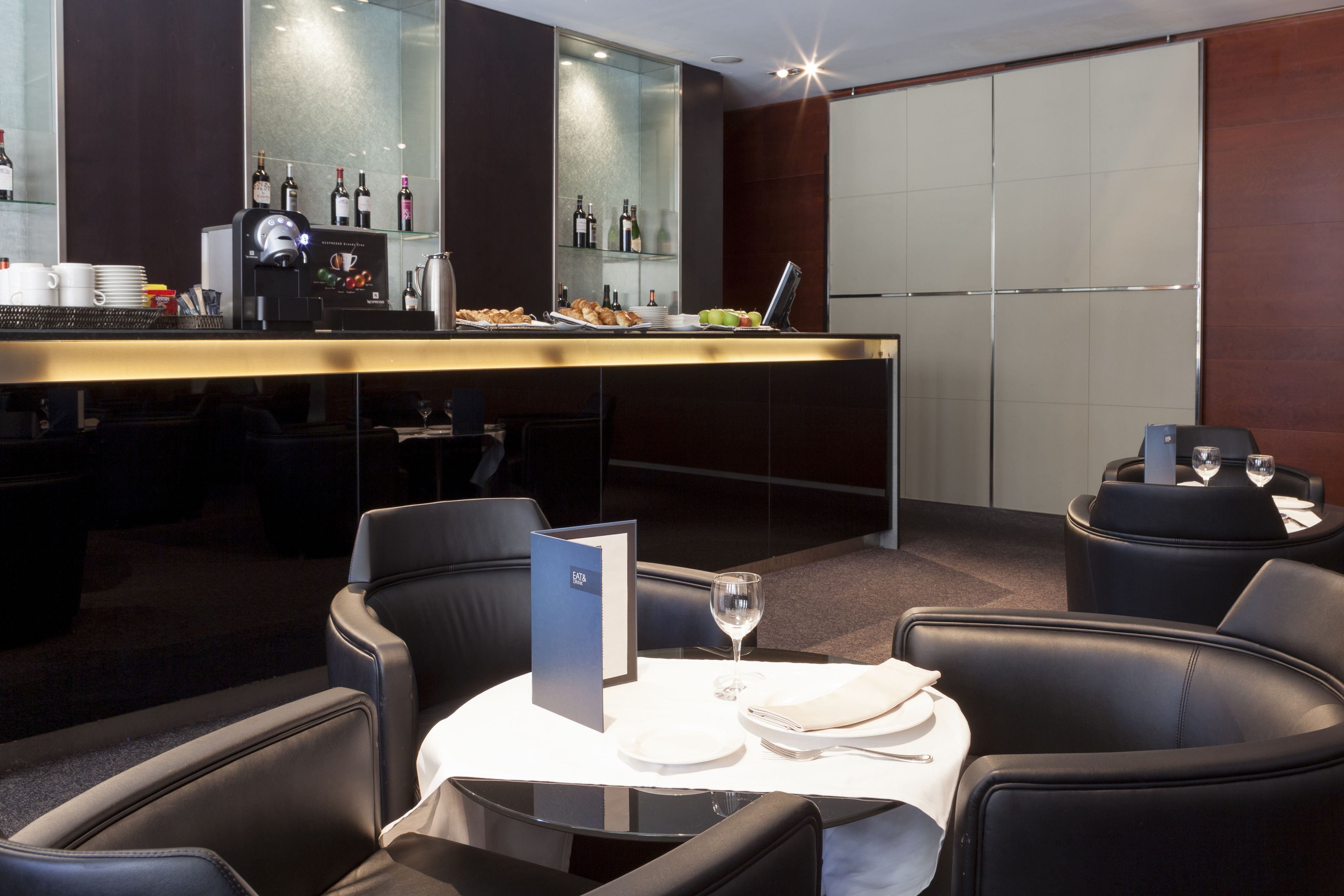 A modern bar area with a coffee machine, wine bottles, and a menu stand.