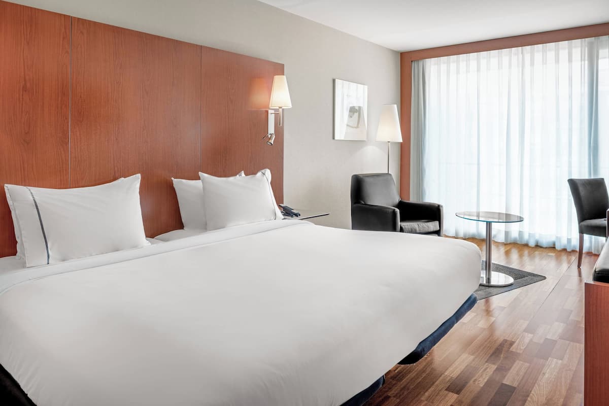 A large bed with white linens, a wooden headboard, two wall-mounted lamps, a small round table, and two chairs in a hotel room.
