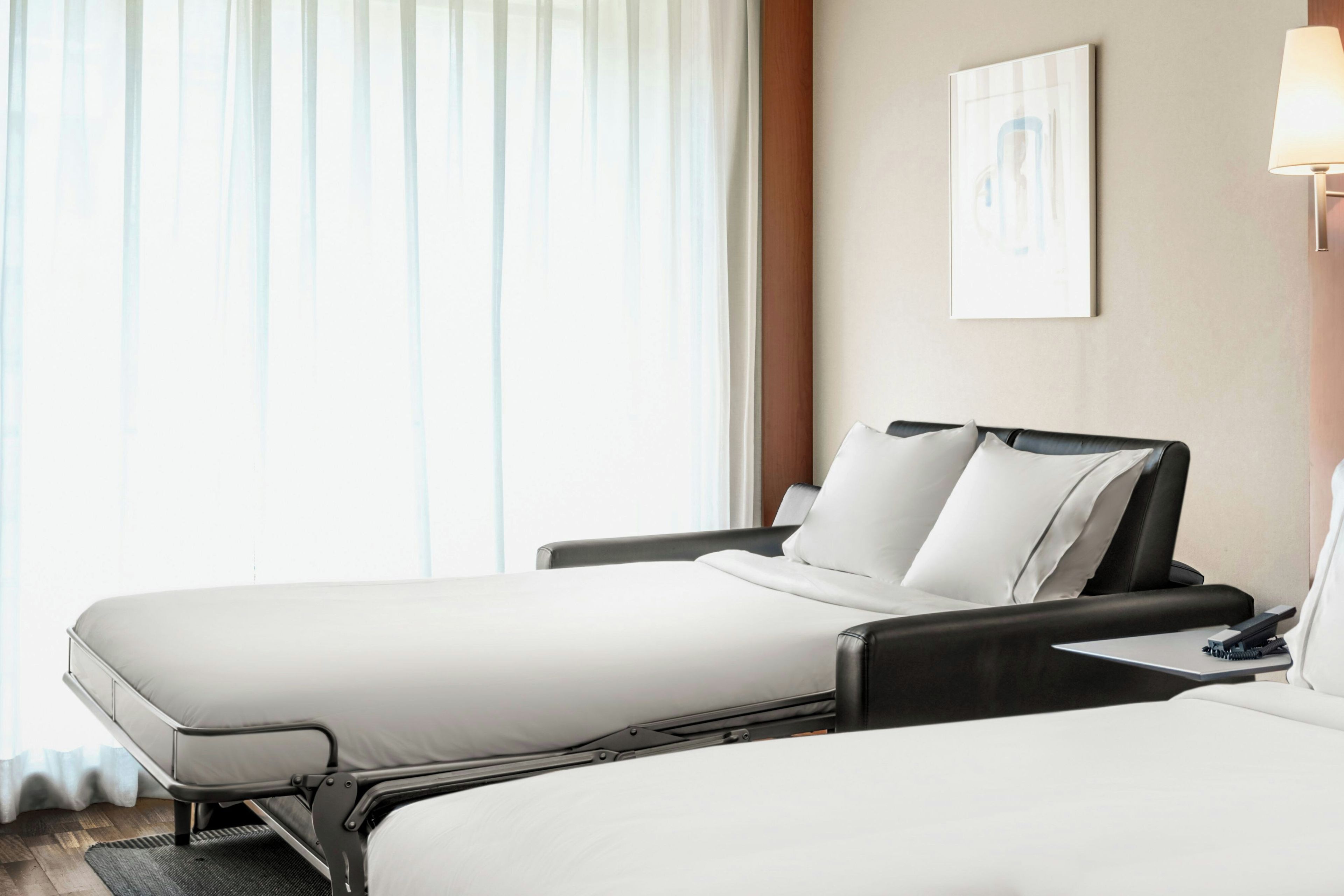 A hotel room with two beds, a desk, a chair, a lamp, and a painting on the wall.