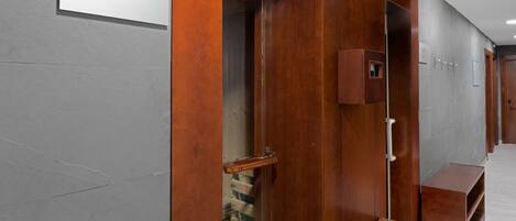 Uma porta de madeira com a inscrição 'SAUNA' que dá acesso a um espaço com um banco e um pequeno armário.
