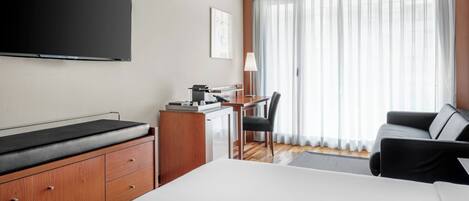 Una habitación de hotel con cama, escritorio, silla, televisión y un ventanal con cortinas.