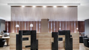 Un espace d’accueil au design moderne, comprenant un comptoir d’accueil en bois, des éléments décoratifs verticaux noirs et un éclairage suspendu.