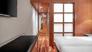 Une chambre d’hôtel avec un plancher en bois, un lit, une télévision et une porte coulissante dotée de panneaux en verre dépoli.