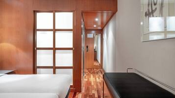 Habitación de hotel con puerta de madera, cama, banco y una obra de arte colgada en la pared.
