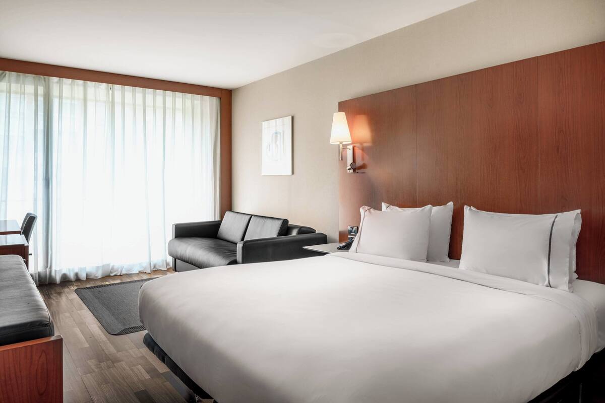 A hotel room with a large bed, a sofa, a desk, and a lamp.