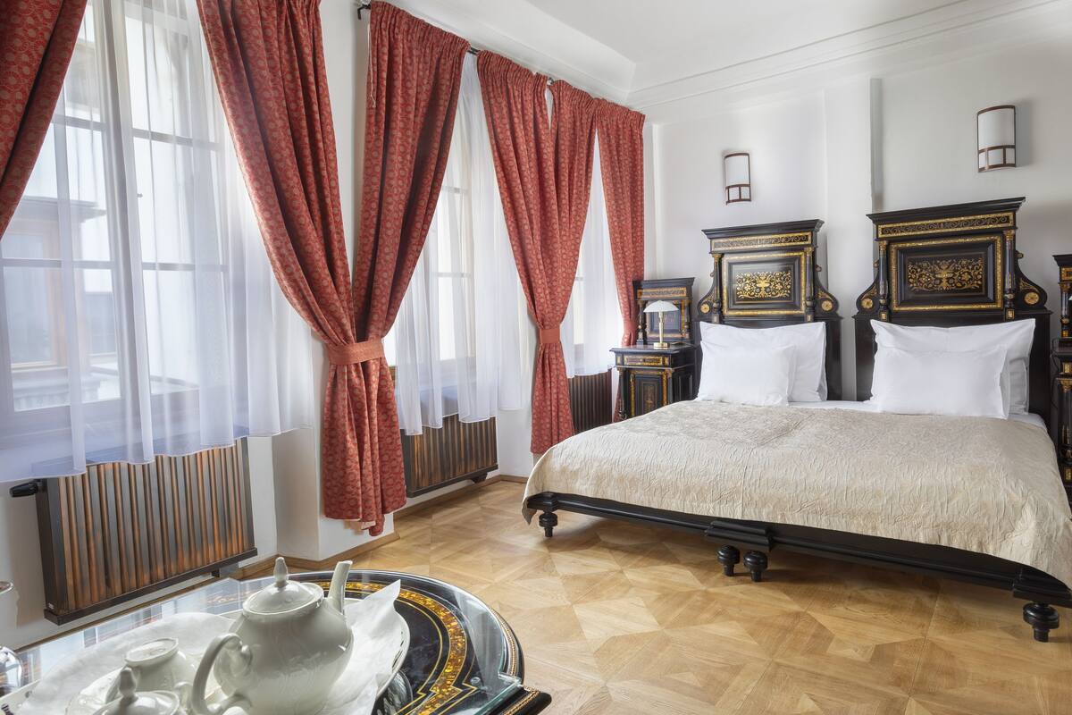 A bedroom with a large bed, two bedside tables, a radiator, and a window with curtains.