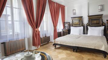 A bedroom with a large bed, two bedside tables, a radiator, and a window with curtains.