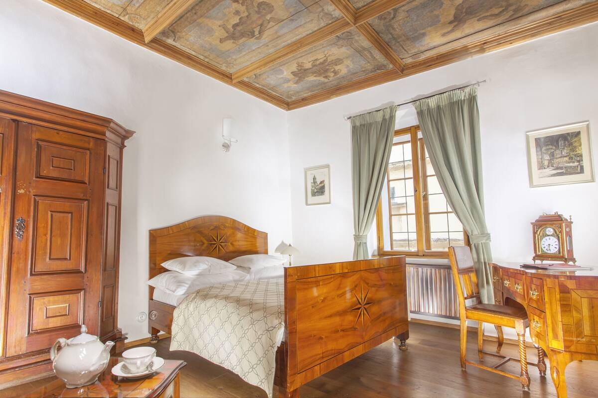 A bedroom with a wooden bed, a wooden desk, a radiator, and a window with curtains.