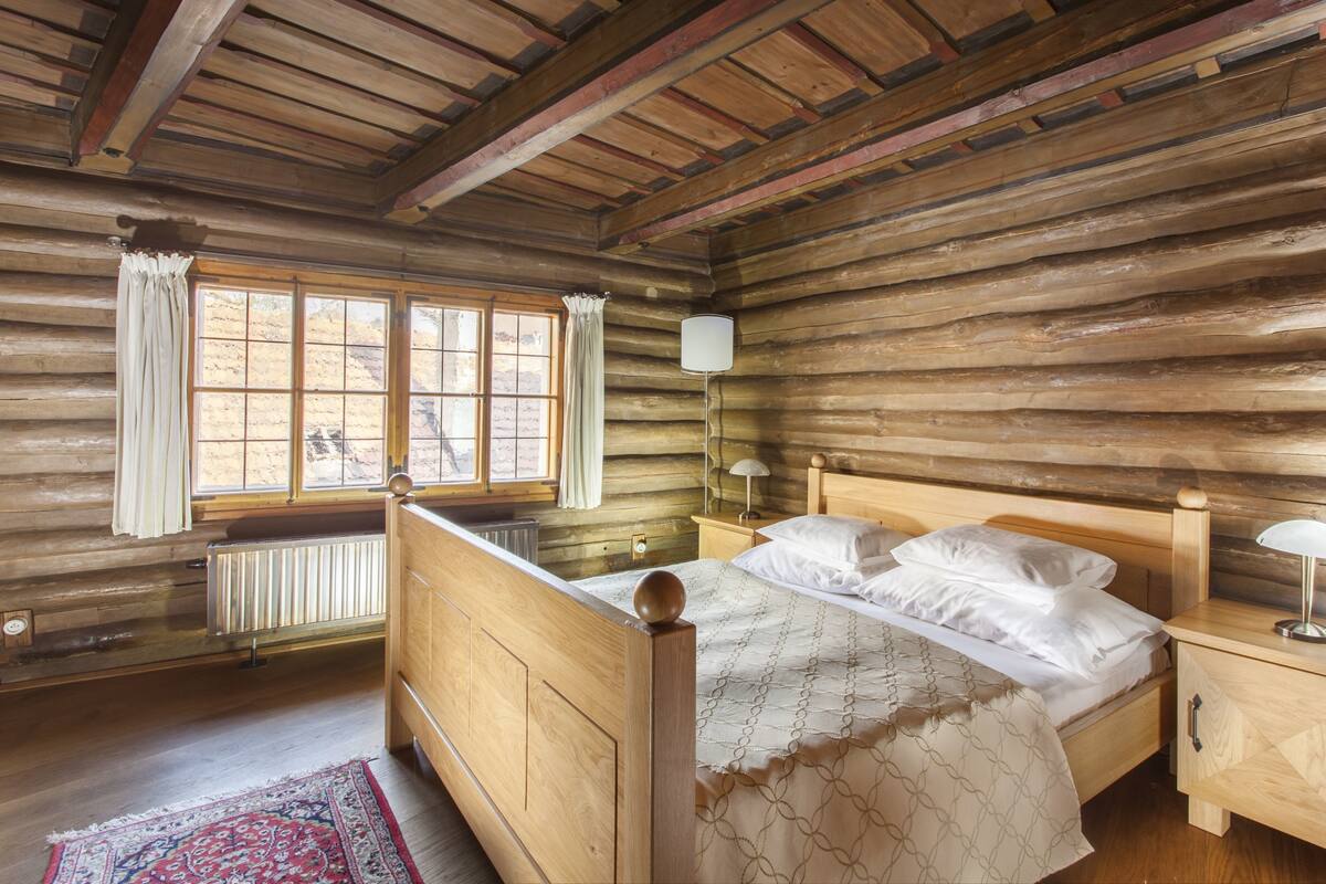 A log cabin bedroom with a wooden bed, nightstands, and a window with curtains.