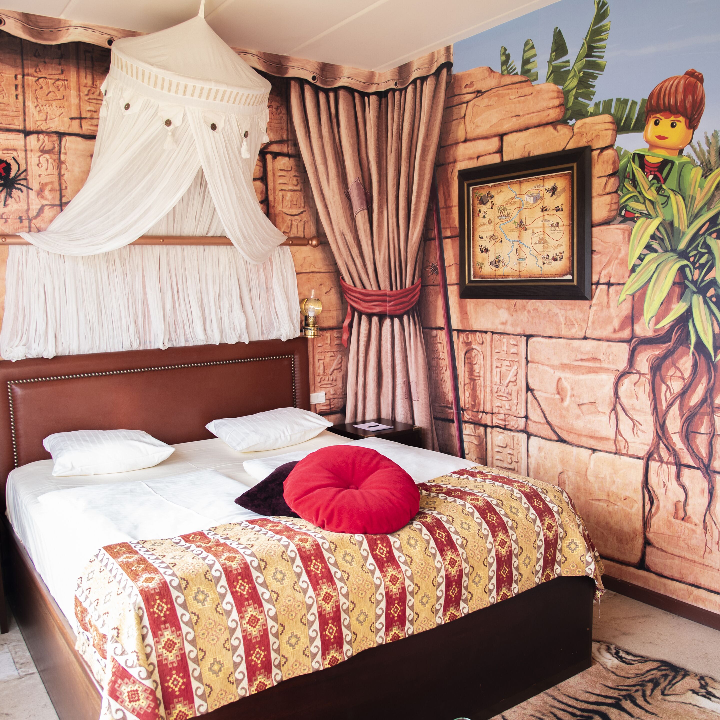 A bed with a patterned bedspread, a red pillow, and a canopy.