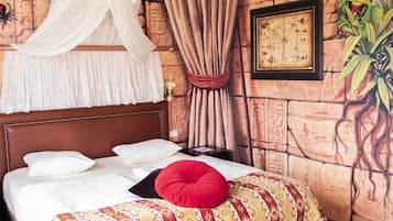 Una cama con colcha estampada, almohada roja y dosel.