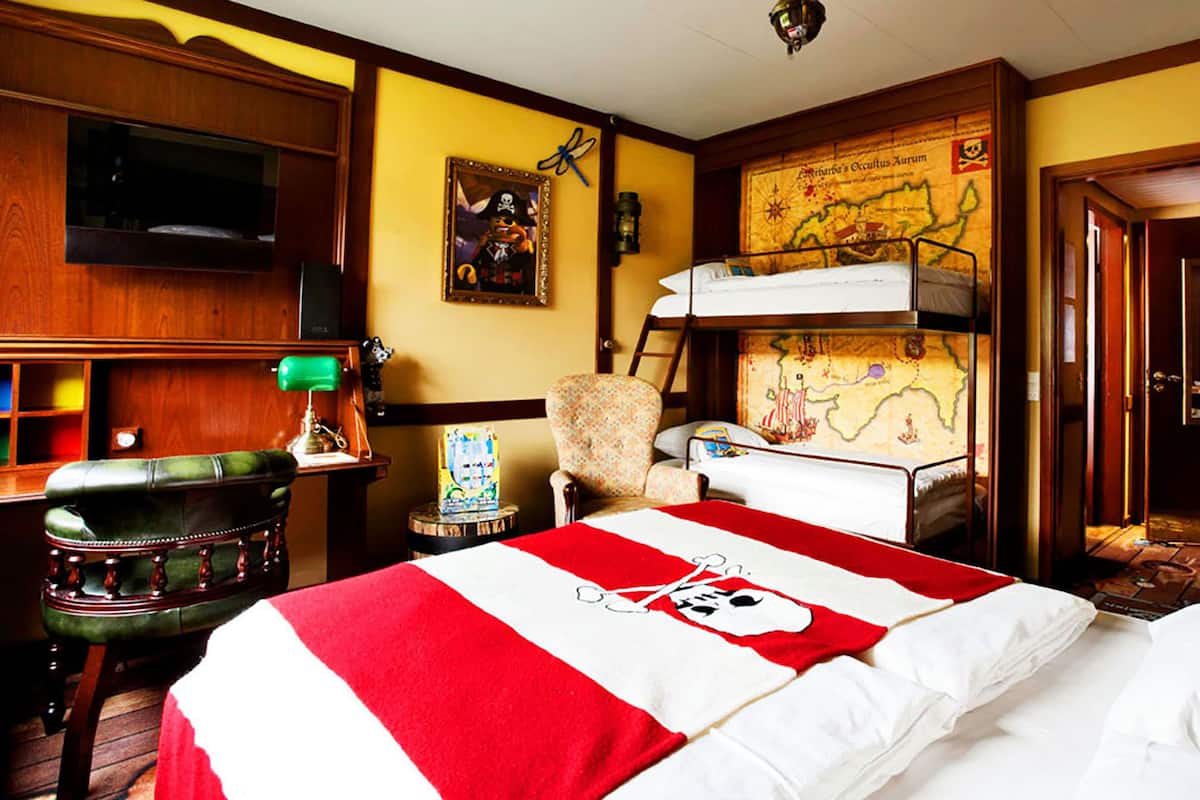 A room with a bunk bed, a desk with a lamp, a map on the wall, and a stuffed toy on the dresser.