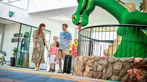 Una familia parada en un espacio interior moderno con una gran escultura de dinosaurio verde.