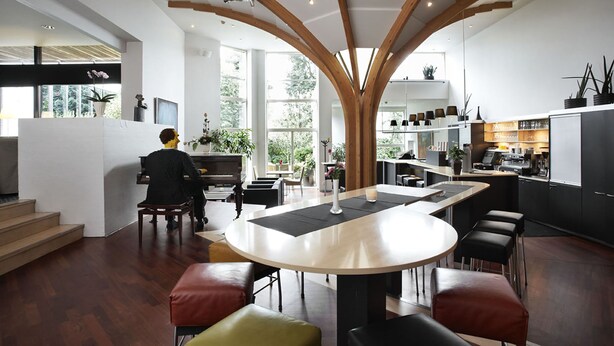 Una cocina moderna con una isla central, vigas de madera y un piano al fondo.