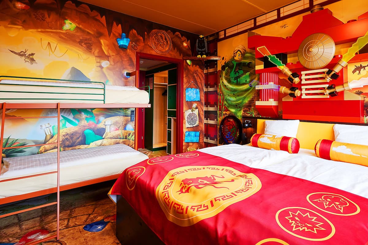 A room with a bunk bed, a mural on the wall, and a bed with a red and yellow bedspread.