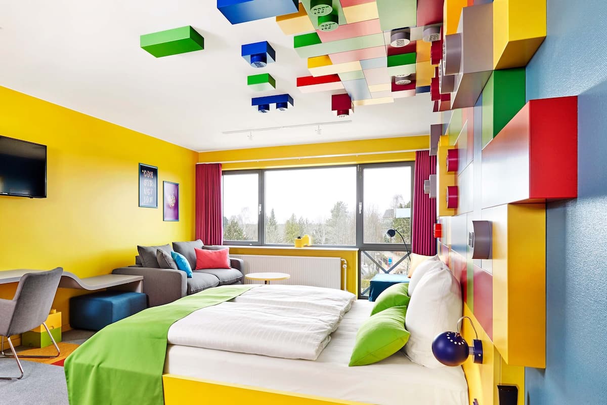 A modern, brightly colored bedroom with a bed, a desk, and a large window.