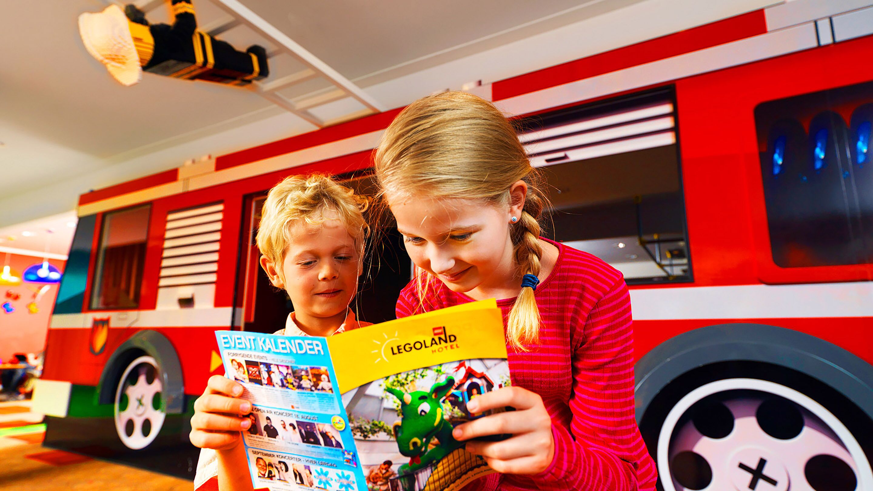 Dos personas leyendo un folleto frente a un autobús rojo.