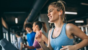Una persona corriendo en una cinta de correr en un gimnasio, con otras personas al fondo.