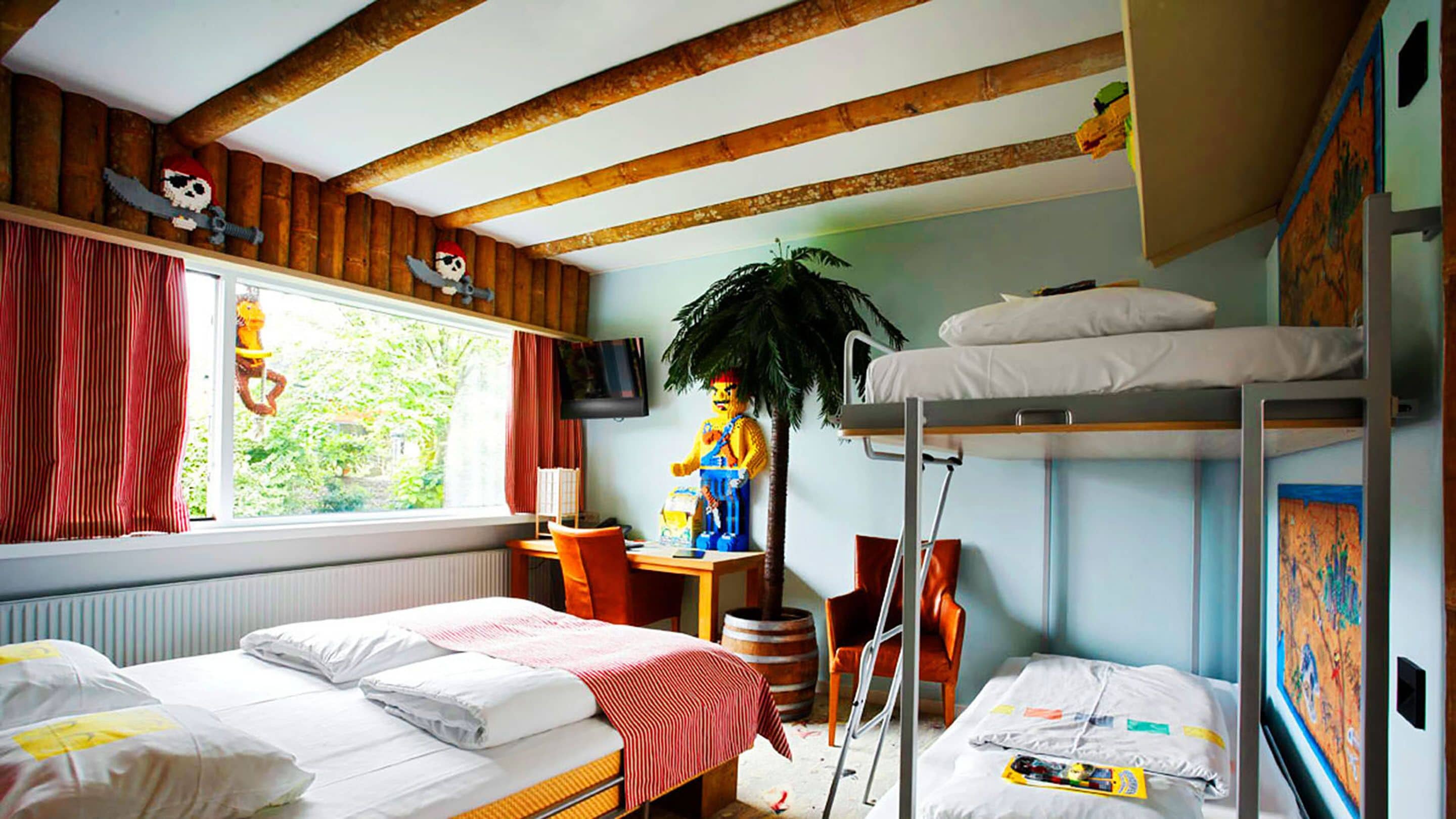 Una habitación con dos camas, una litera, un escritorio con silla, una televisión y una ventana con cortinas.