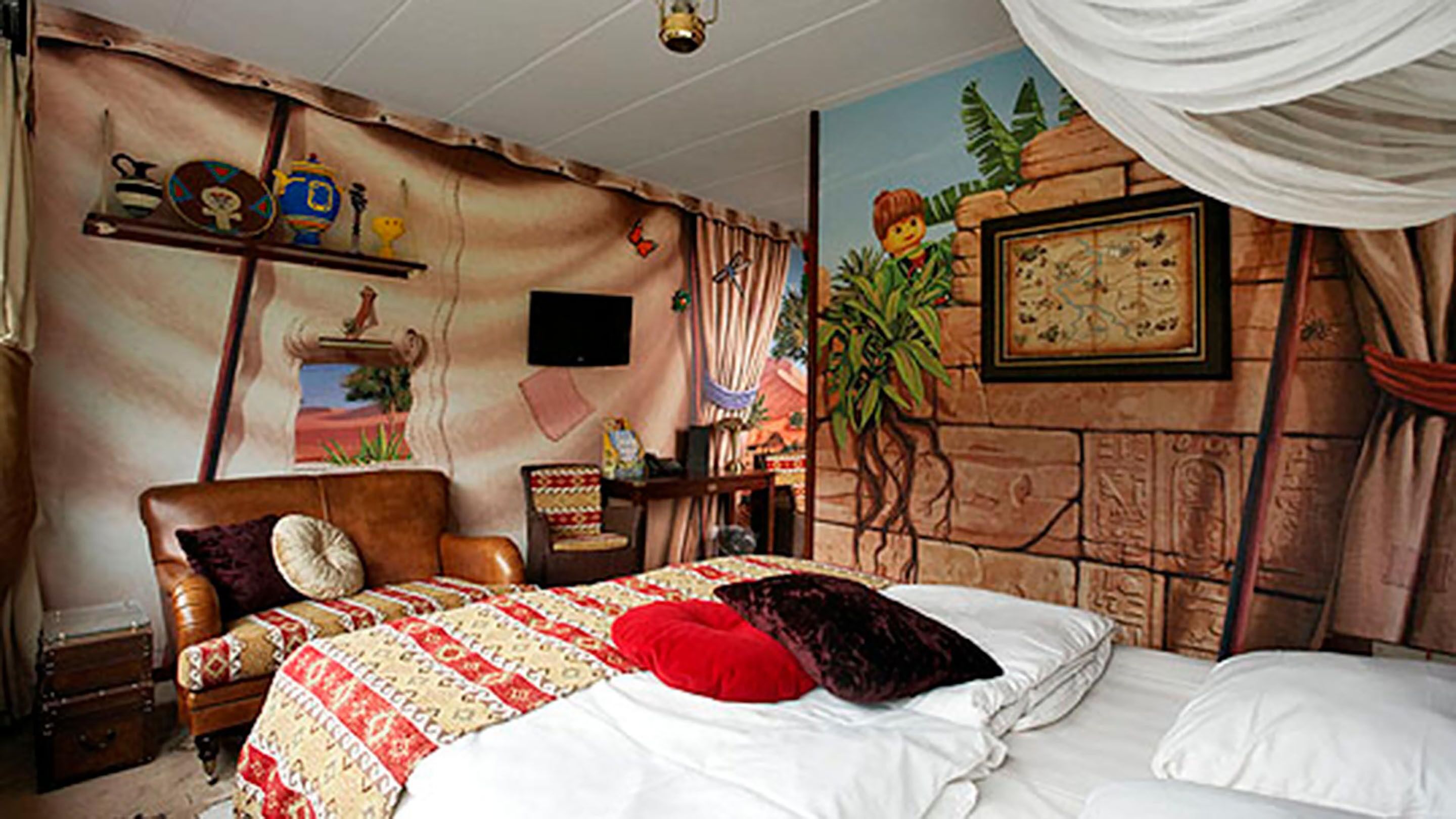 A bedroom with a bed, pillows, a dresser, a nightstand, a lamp, a map on the wall, and a window with curtains.