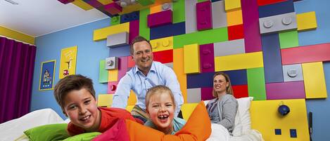A room with a colorful LEGO wall, a bed with pillows, and a nightstand with a lamp.