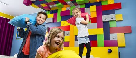 Une pièce avec un mur décoré de briques LEGO aux couleurs vives, un lit et un bureau avec une lampe.