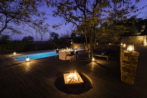 A wooden deck with a pool, outdoor seating, and a fire pit.