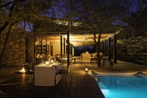 Un espacio exterior para comer con piscina, paredes de piedra y una zona cubierta con asientos.