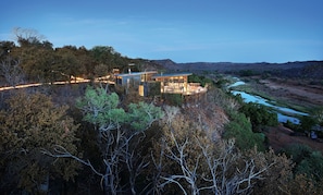 A modern house with a deck overlooking a river and forested hills.