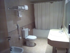 A bathroom with a toilet, bidet, and bathtub. There are towels and toiletries on the wall.