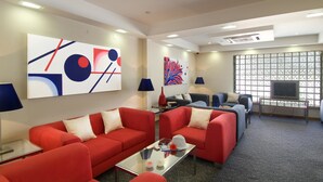 A modern hotel room with red sofas, a glass coffee table, abstract wall art, a flat-screen TV, and a patterned carpet. - Cruz Alta (Ourem)