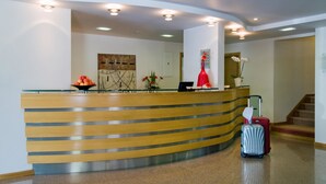A hotel reception desk with a curved design, a red vase, and a suitcase. - Cruz Alta (Ourem)