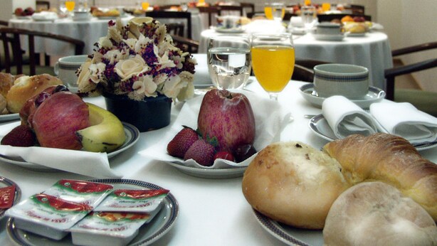 A breakfast setting with various pastries, fruits, and a floral centerpiece on a table. - Cruz Alta (Ourem)