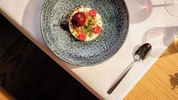 Een blauw keramieken bord met een dessert op een witte tafel, met een lepel erbij.
