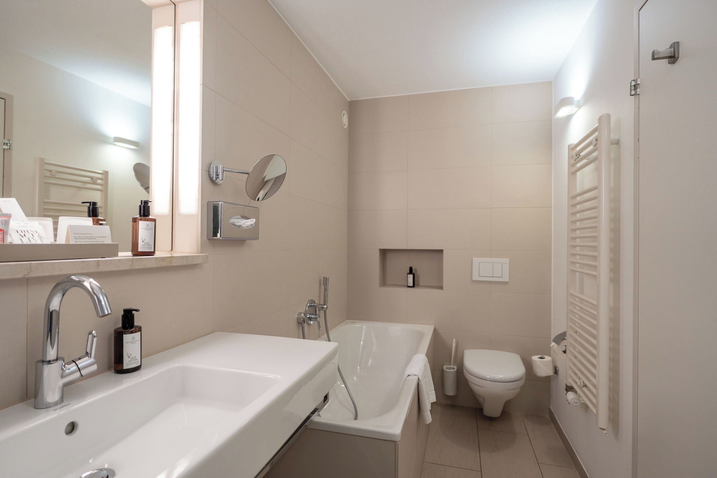Ein modernes Badezimmer mit Waschbecken, Spiegel, Badewanne, Toilette und Handtuchhalter.
