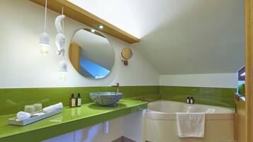 Un baño moderno con encimera verde, un espejo ovalado grande, una bañera independiente y un aplique de pared.