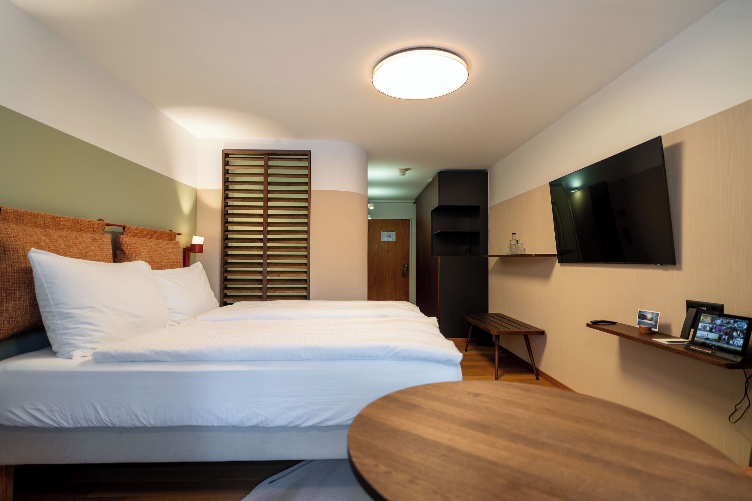 A modern hotel room with a bed, a desk, a TV, and a wooden floor.