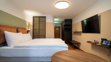 A modern hotel room with a bed, a desk, a TV, and a wooden floor.