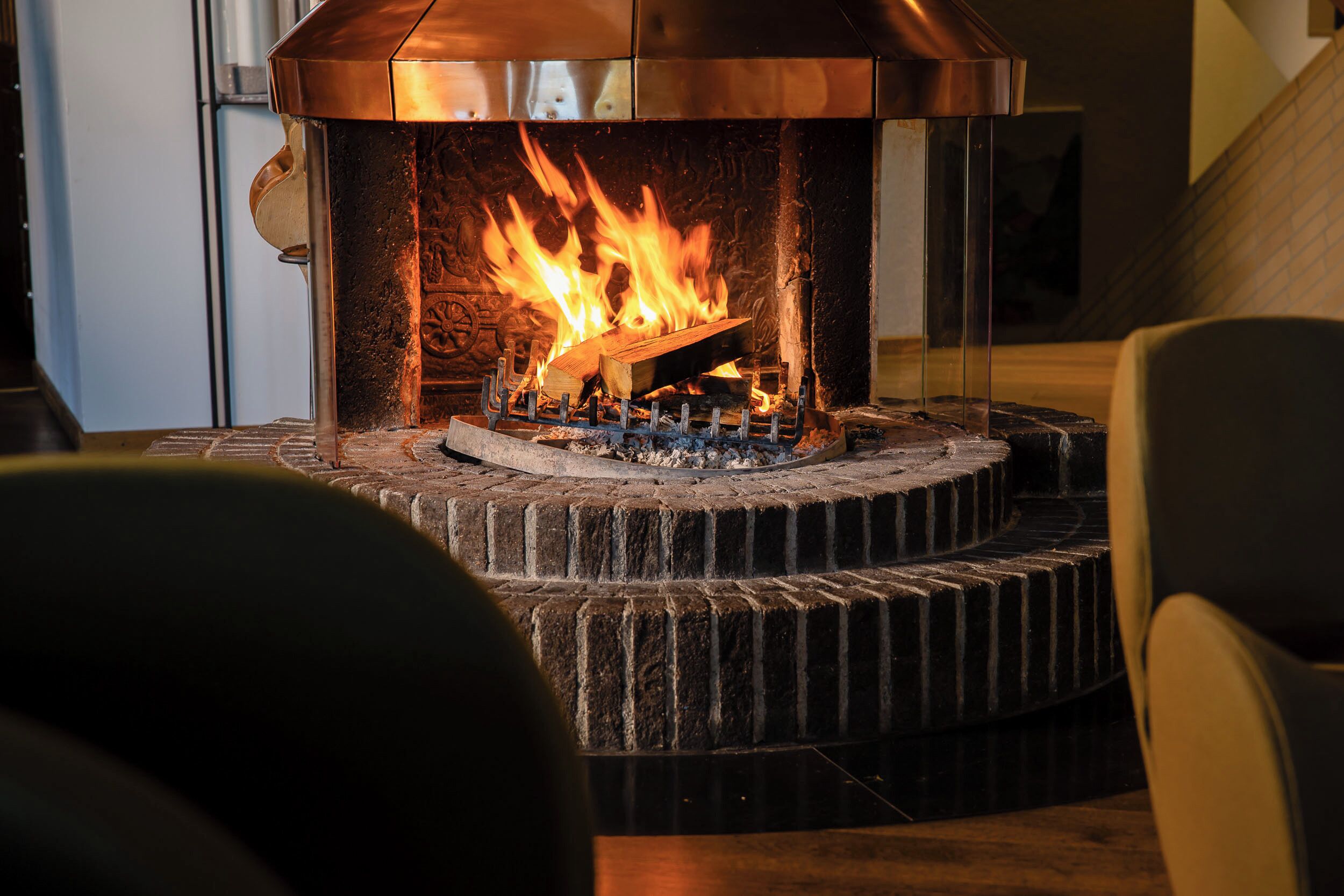 Una chimenea con un marco de piedra y una cubierta metálica, con llamas visibles en su interior.