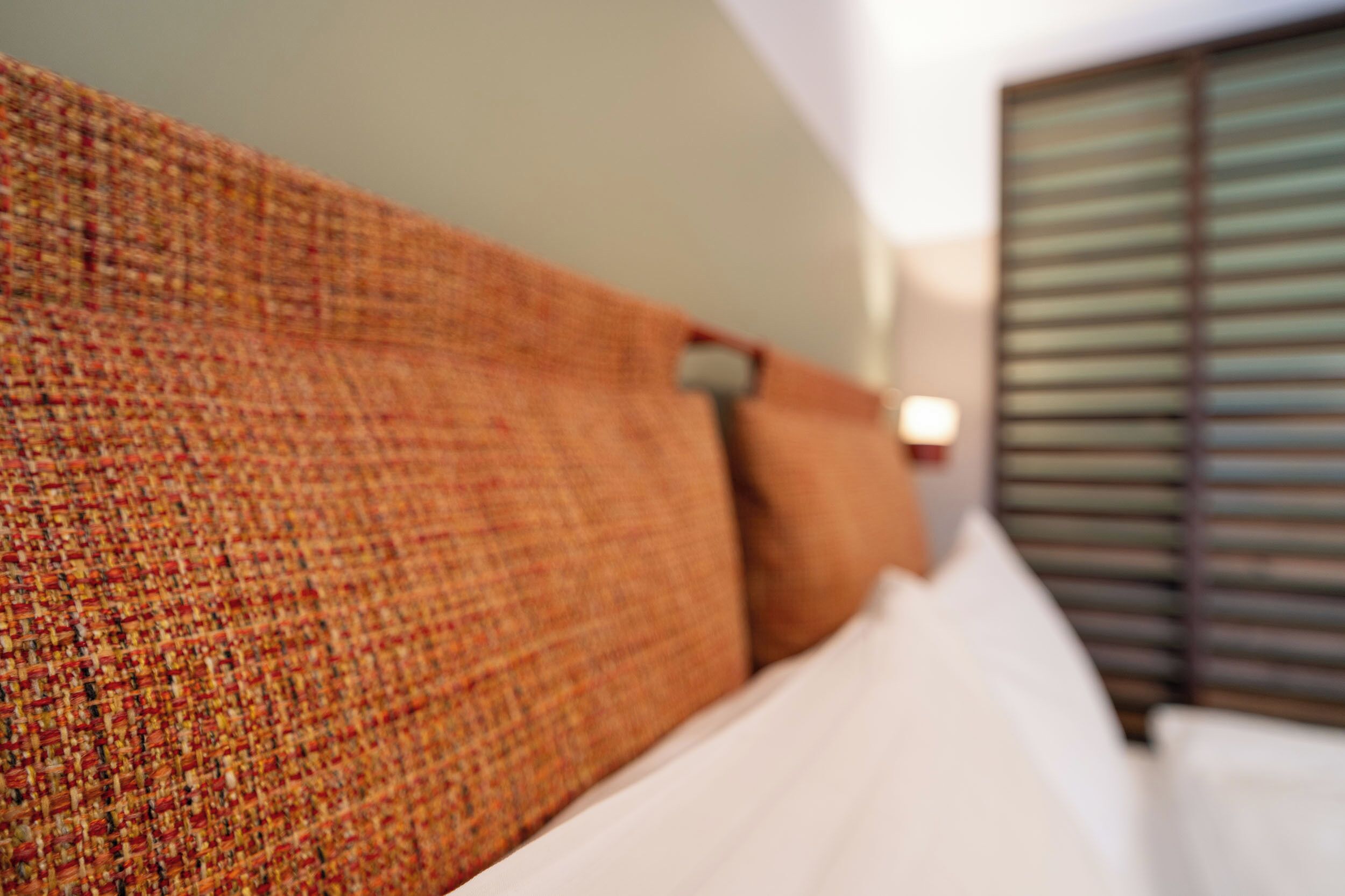 Una cama con cabecera texturizada, almohadas blancas y una ventana con persianas.
