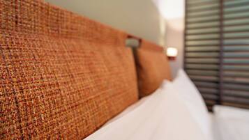 Una cama con cabecera texturizada, almohadas blancas y una ventana con persianas.