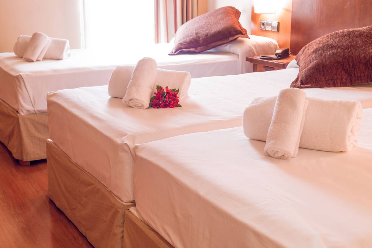 A hotel room with two beds, each with neatly folded towels and a small bouquet of flowers.