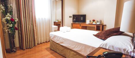 Habitación de hotel con cama, mesita de noche, televisión y un jarrón con flores.