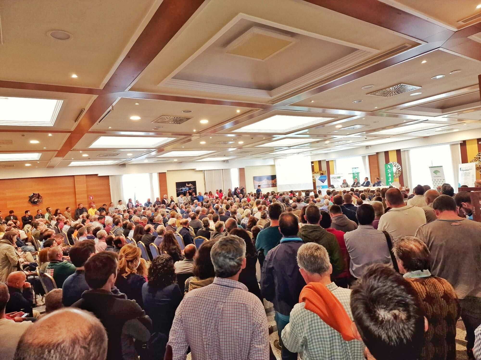 A large conference room with a high ceiling, recessed lighting, and a stage at the front.