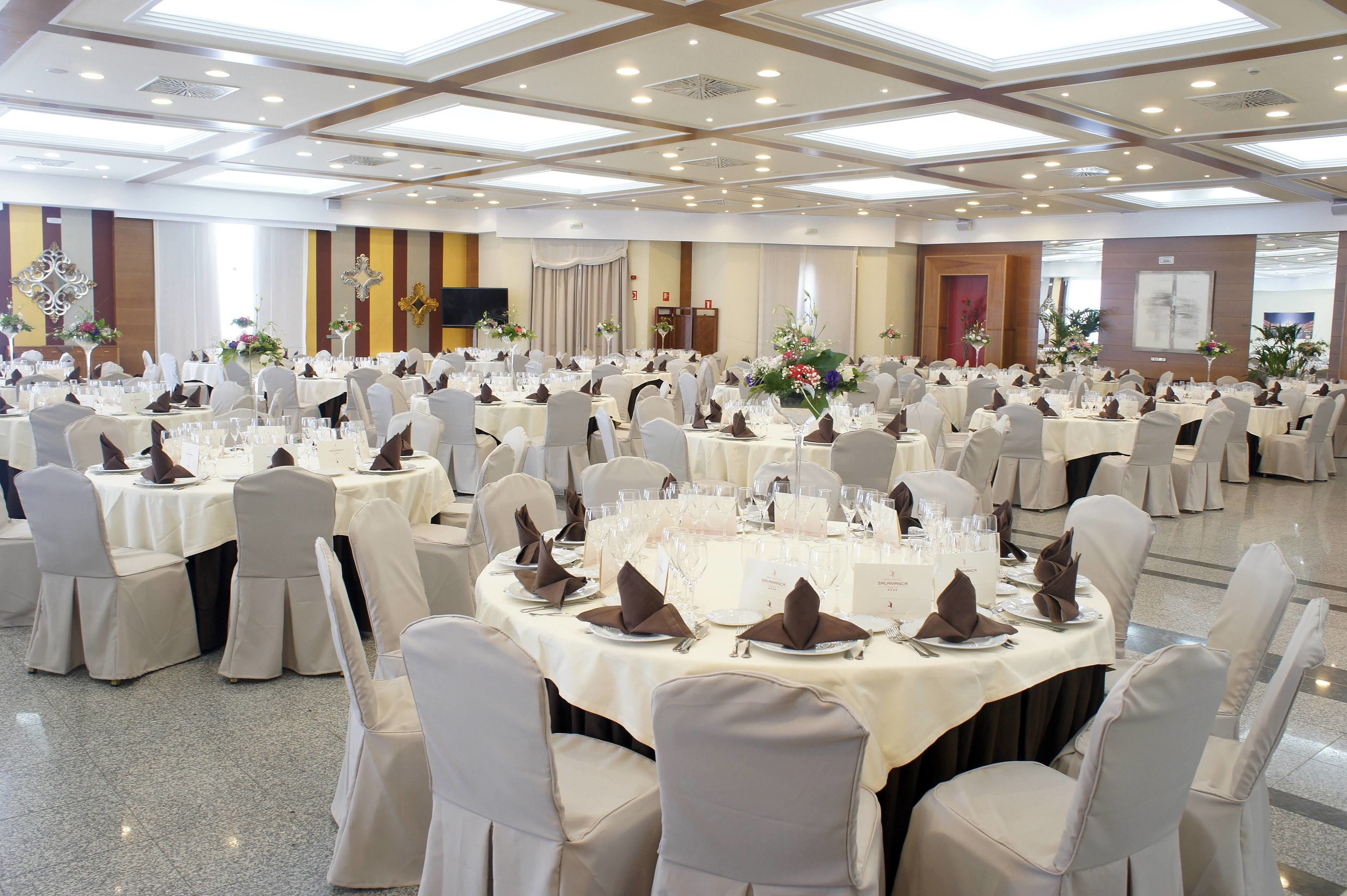 A banquet hall with round tables set for a formal event, featuring white tablecloths, folded napkins, and floral centerpieces.