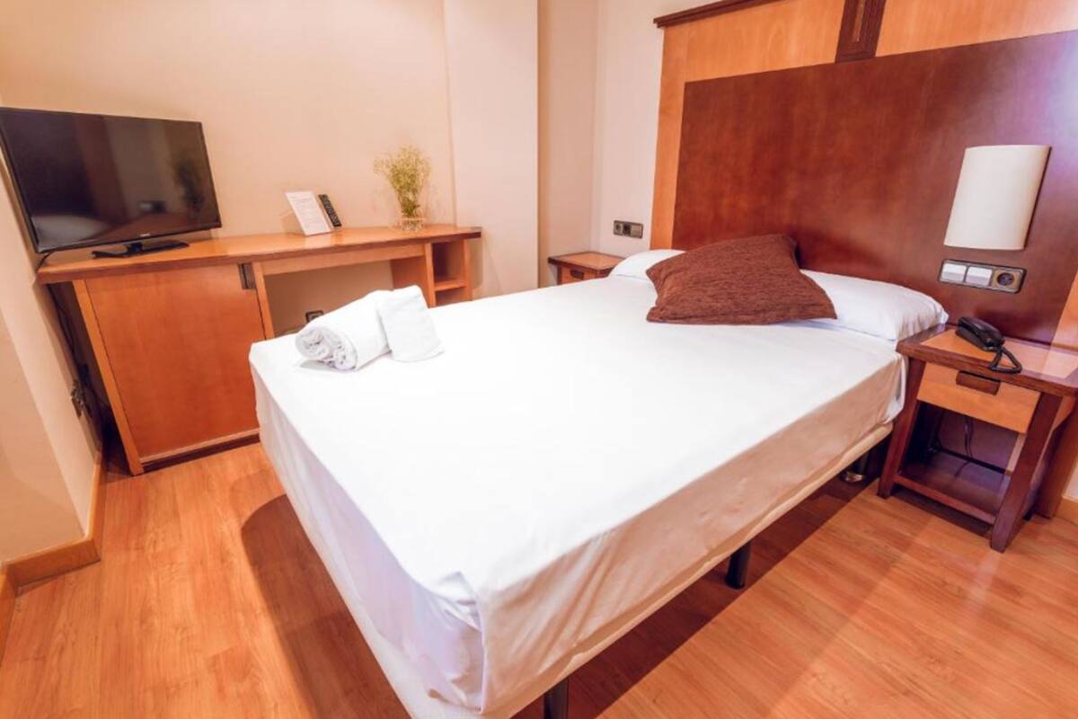 A hotel room with a bed, a TV, a desk, and a bedside table.