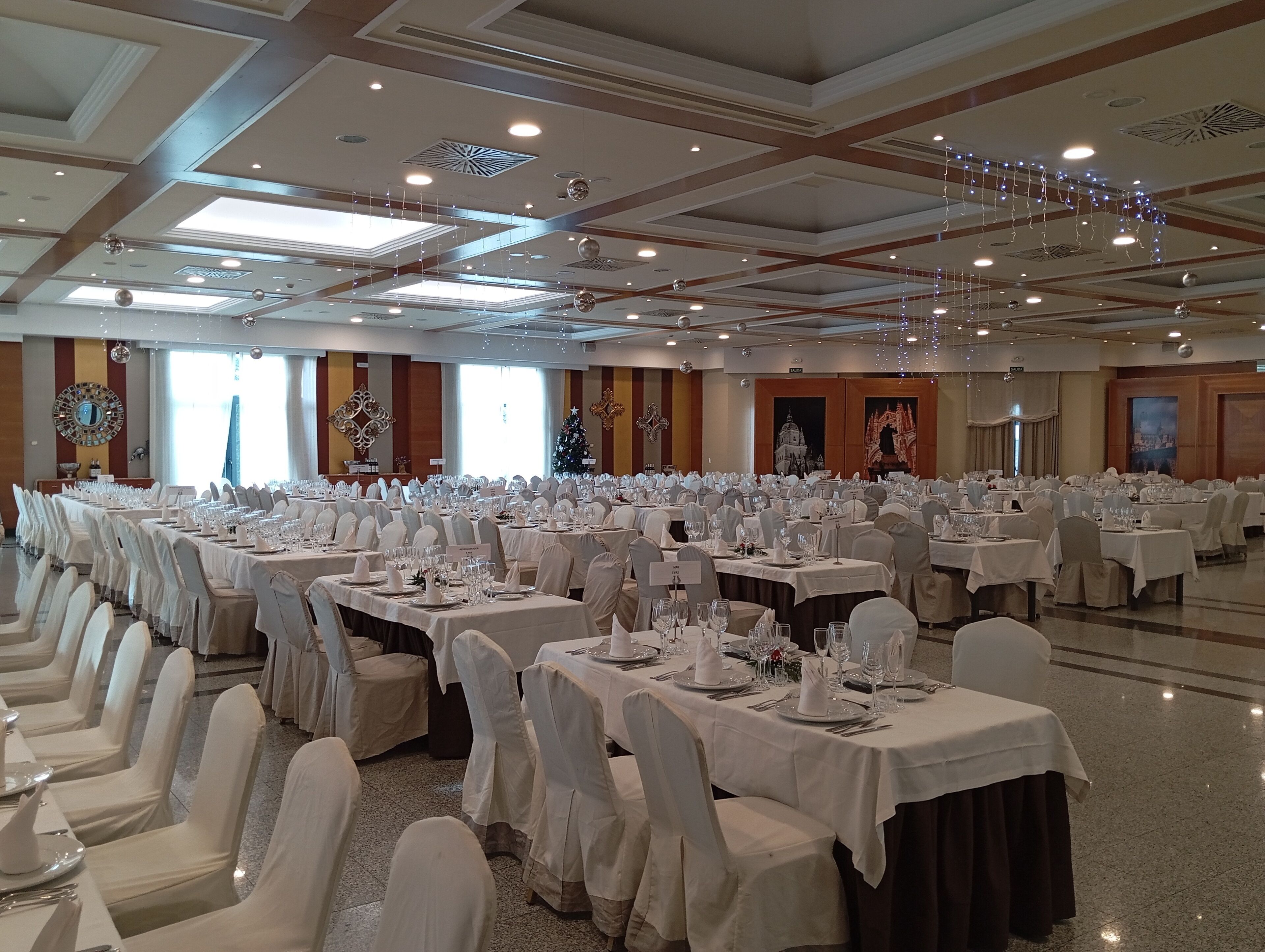 A large banquet hall with rows of tables set for a formal event, featuring chandeliers and decorative lighting.