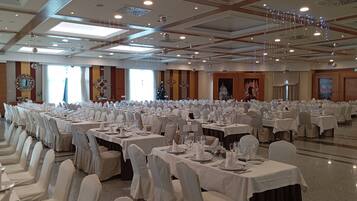 A large banquet hall with rows of tables set for a formal event, featuring chandeliers and decorative lighting.